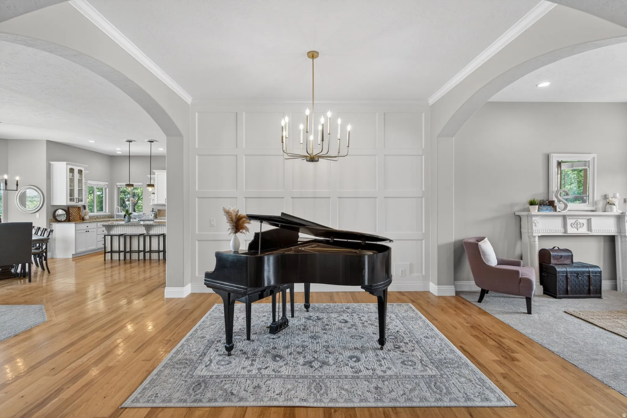 Hardwood flooring throughout featuring a decorative wall paneling accent, an arched doorway, and an ornate white mantelpiece