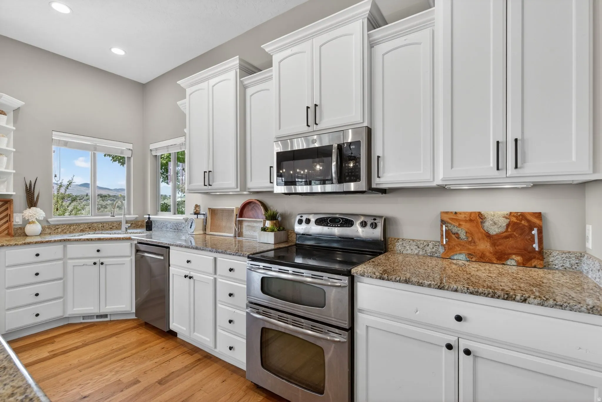 Bright kitchen featuring white cabinetry, light-toned granite countertops and wood-finish flooring