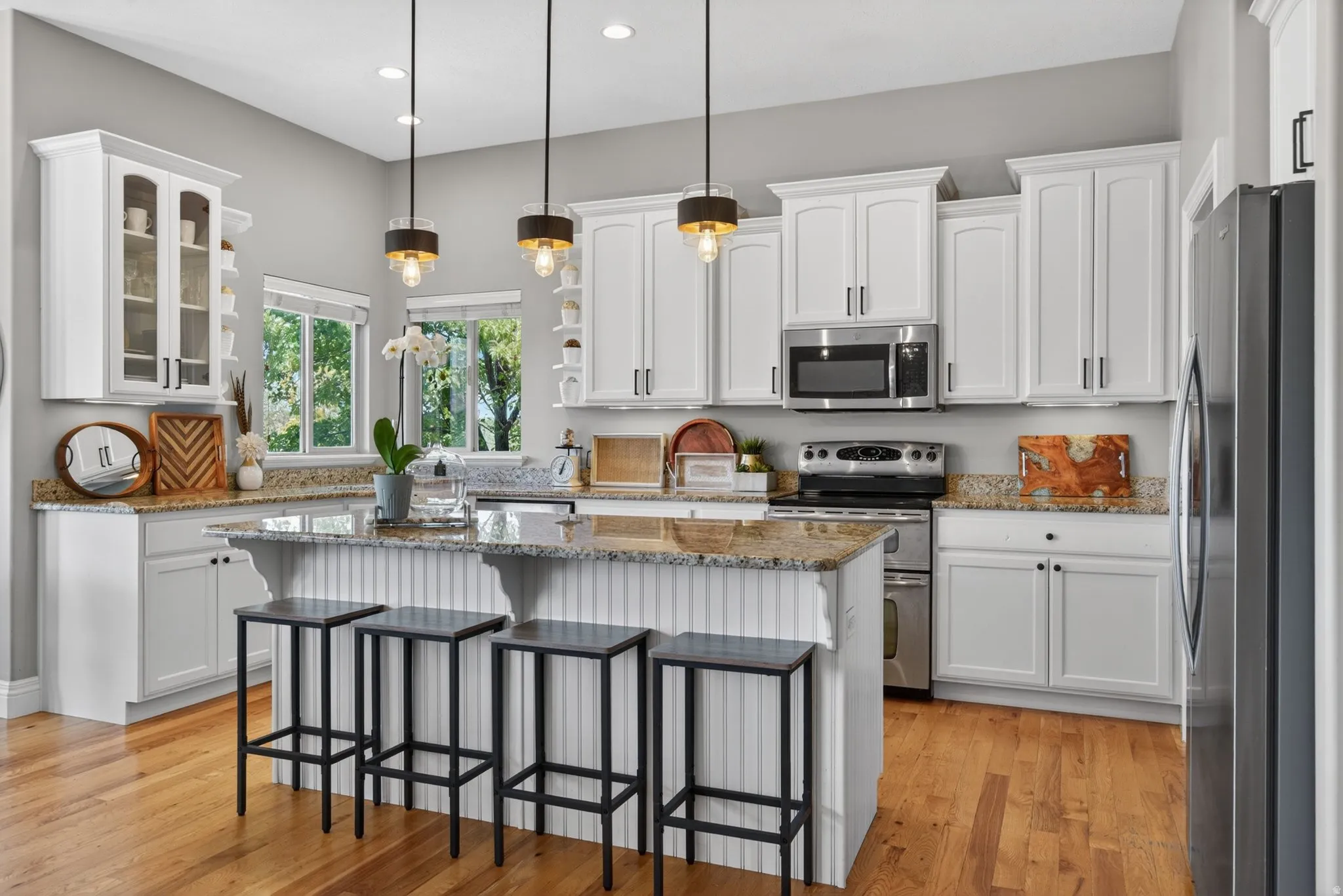 Gourmet kitchen with wood-finish flooring, white cabinetry, granite countertops and a central island with pendant lighting