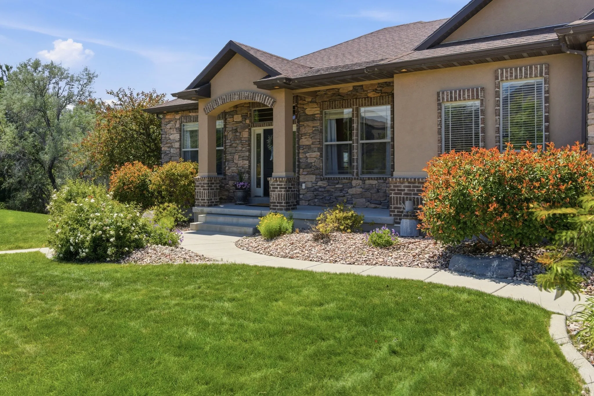 Stucco and stone exterior featuring an arched entryway, gabled roofline, and multiple windows