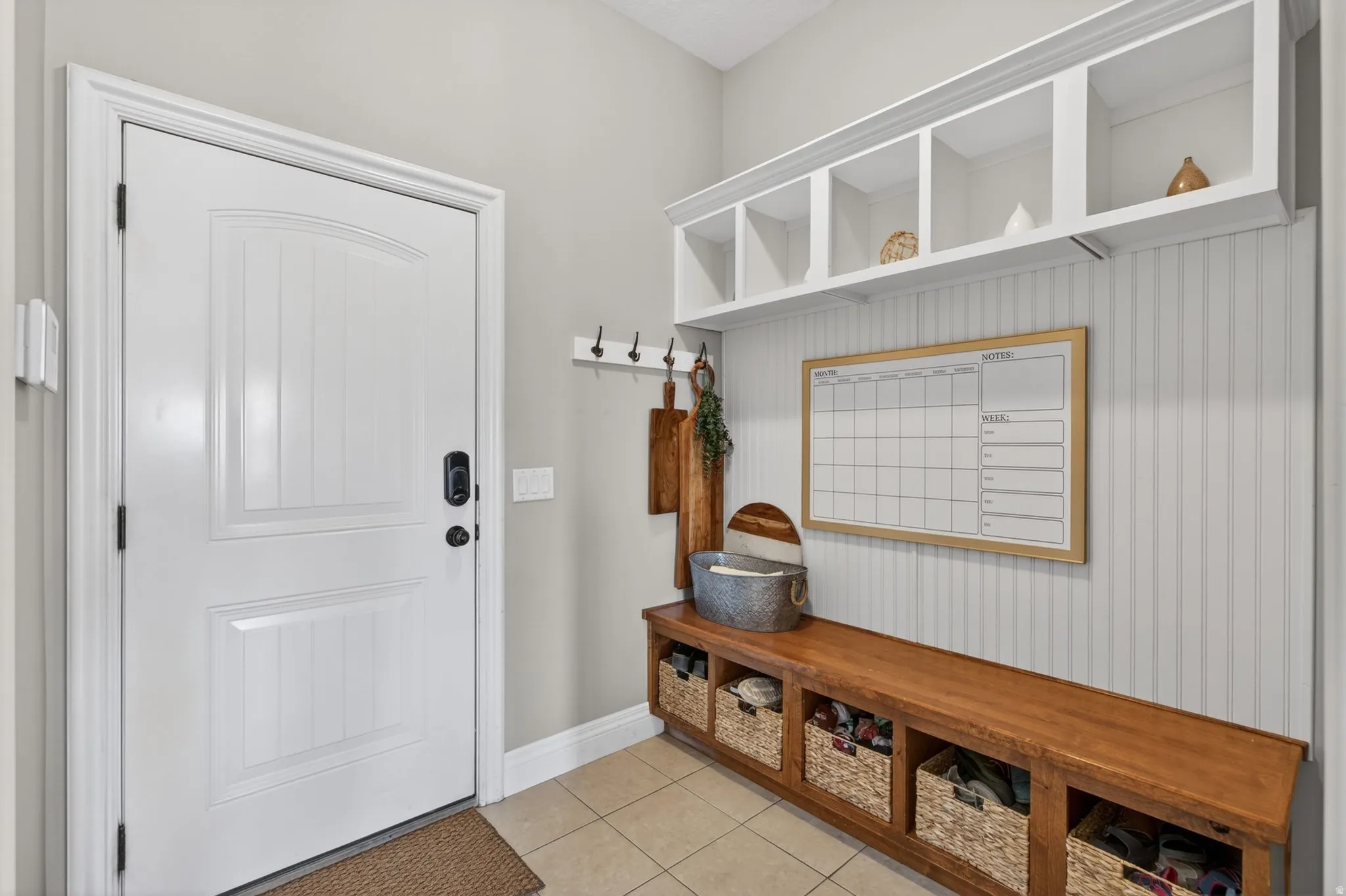 Entryway featuring a white paneled door with smart lock hardware, tiled flooring, and a built-in wood-finish bench with integrated storage cubbies