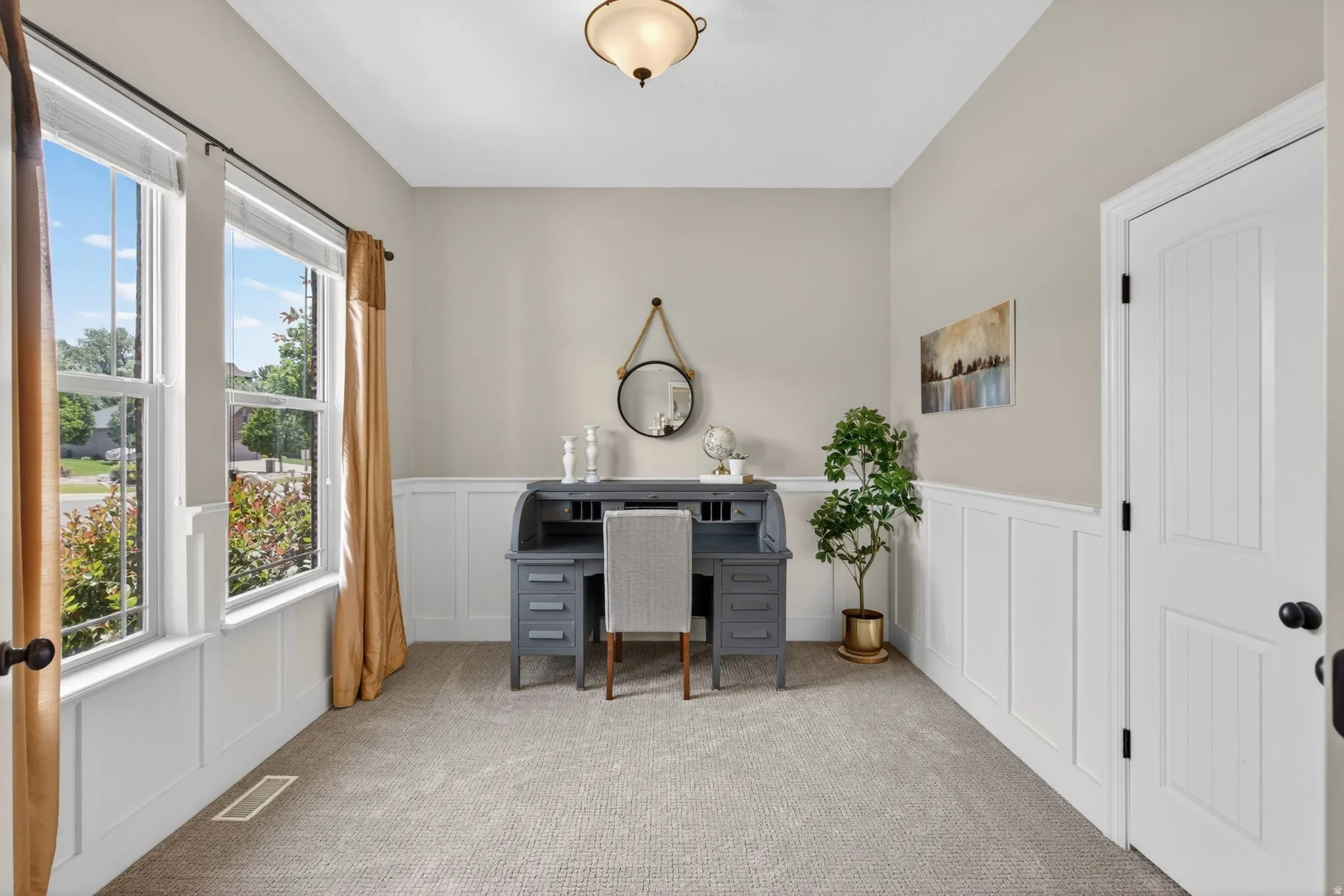 Carpeted room featuring wainscoting, two large windows with trim, a solid panel door, and a ceiling-mounted light fixture