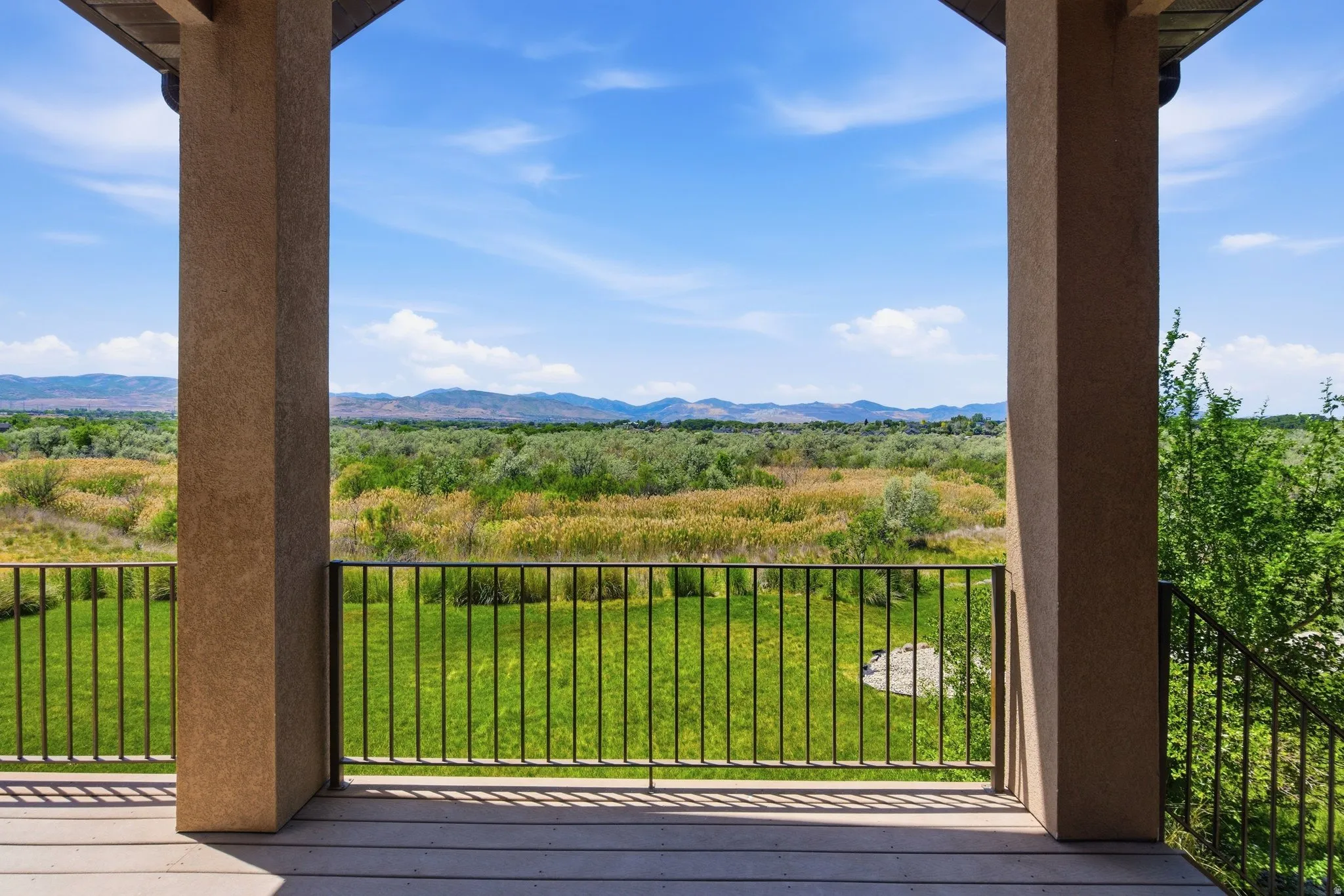 Expansive balcony featuring a composite deck and dark metal railing, overlooking a verdant landscape with distant mountains