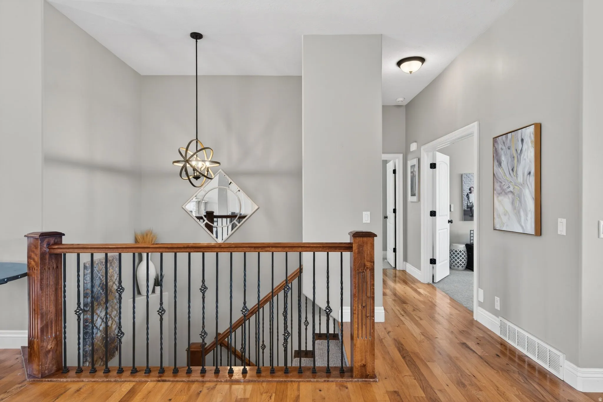 Upper landing featuring wood-finish flooring, a wood banister with wrought iron spindles, and a contemporary spherical light fixture