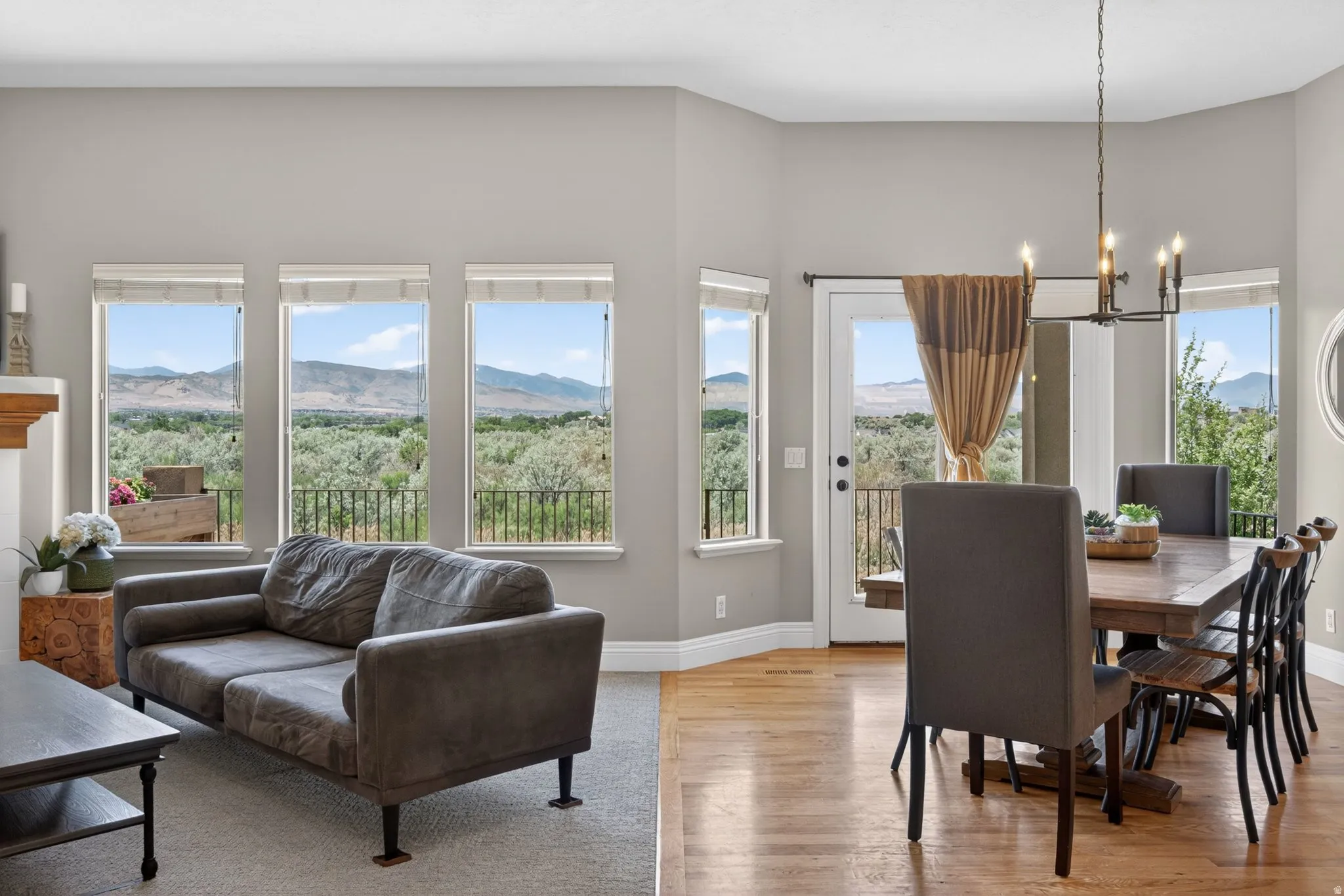 Open-concept living and dining areas featuring multiple windows, a glass-panel door, light hardwood flooring, and a contemporary chandelier