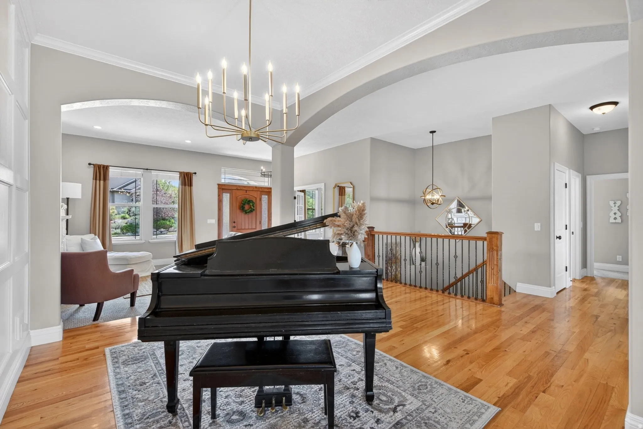 Spacious entry foyer featuring wood-finish flooring, a contemporary chandelier, arched doorways, a built-in paneled wall, and a staircase with wood newel posts and metal balusters