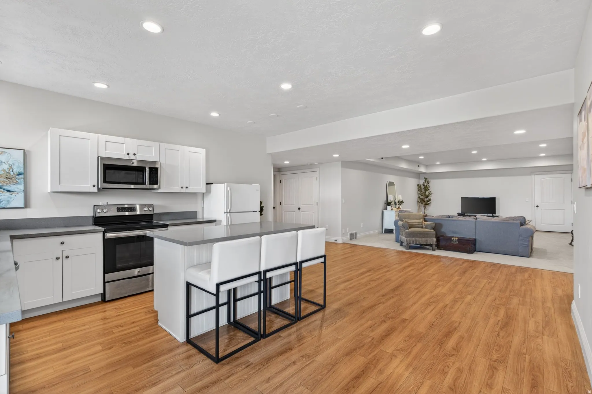 Open-concept living area featuring a kitchen with white cabinetry and  a center island with seating, wood-finish flooring, and recessed lighting