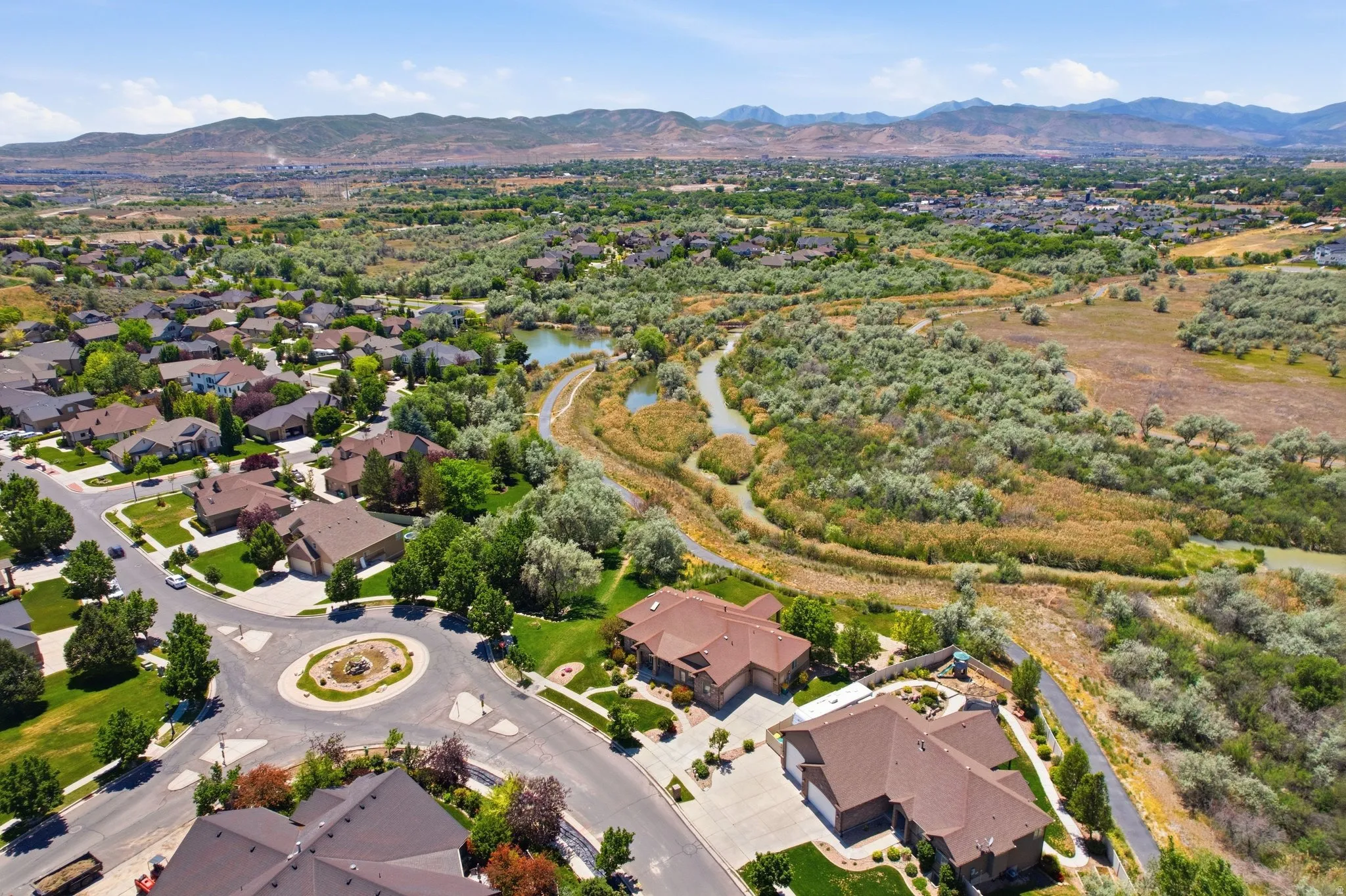 Expansive aerial view showcasing residential properties, a winding natural waterway, and distant mountains