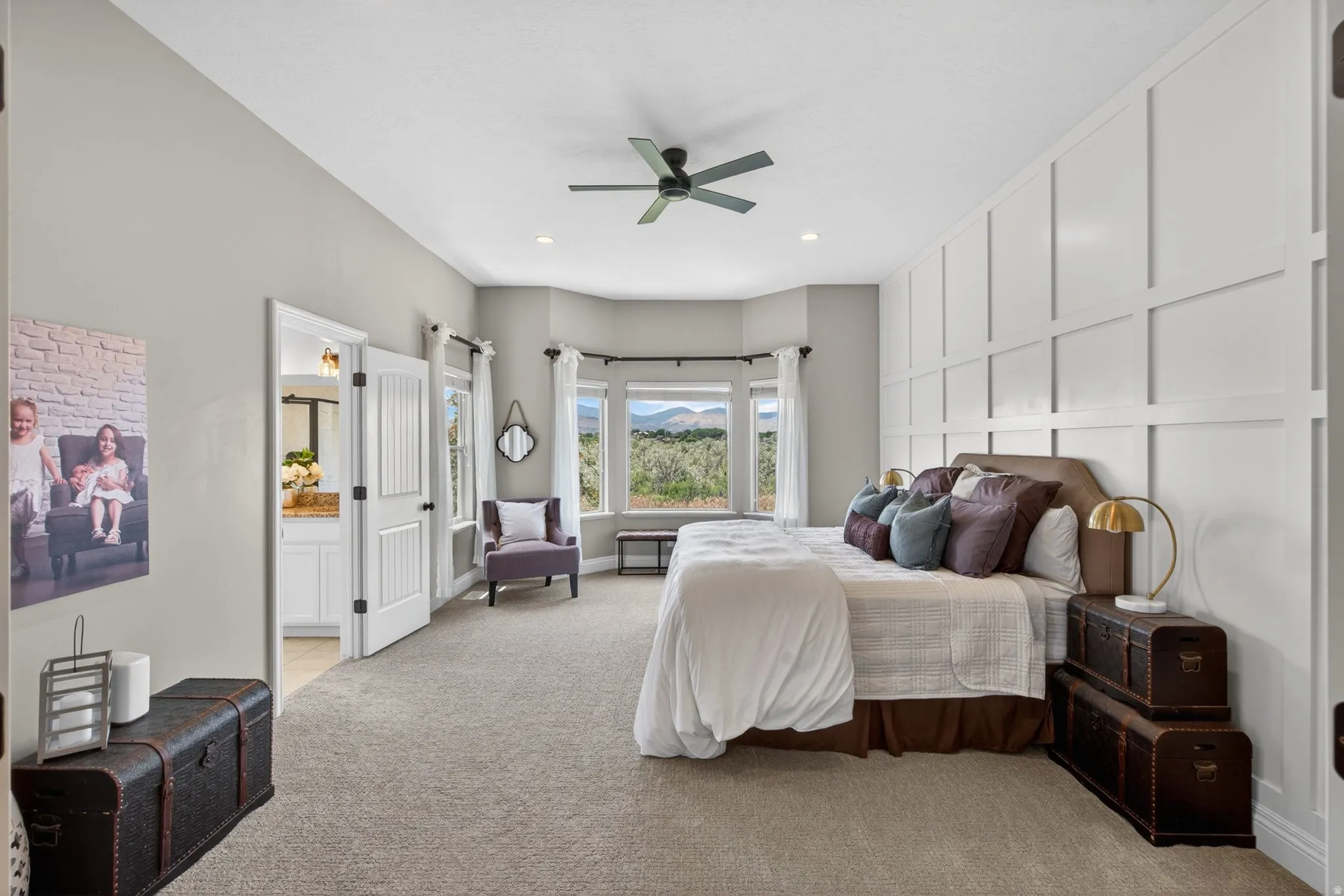 Spacious room featuring a bay window, board and batten accent wall, ceiling fan, recessed lighting, and a doorway opening to a bathroom with a white vanity and stone countertop