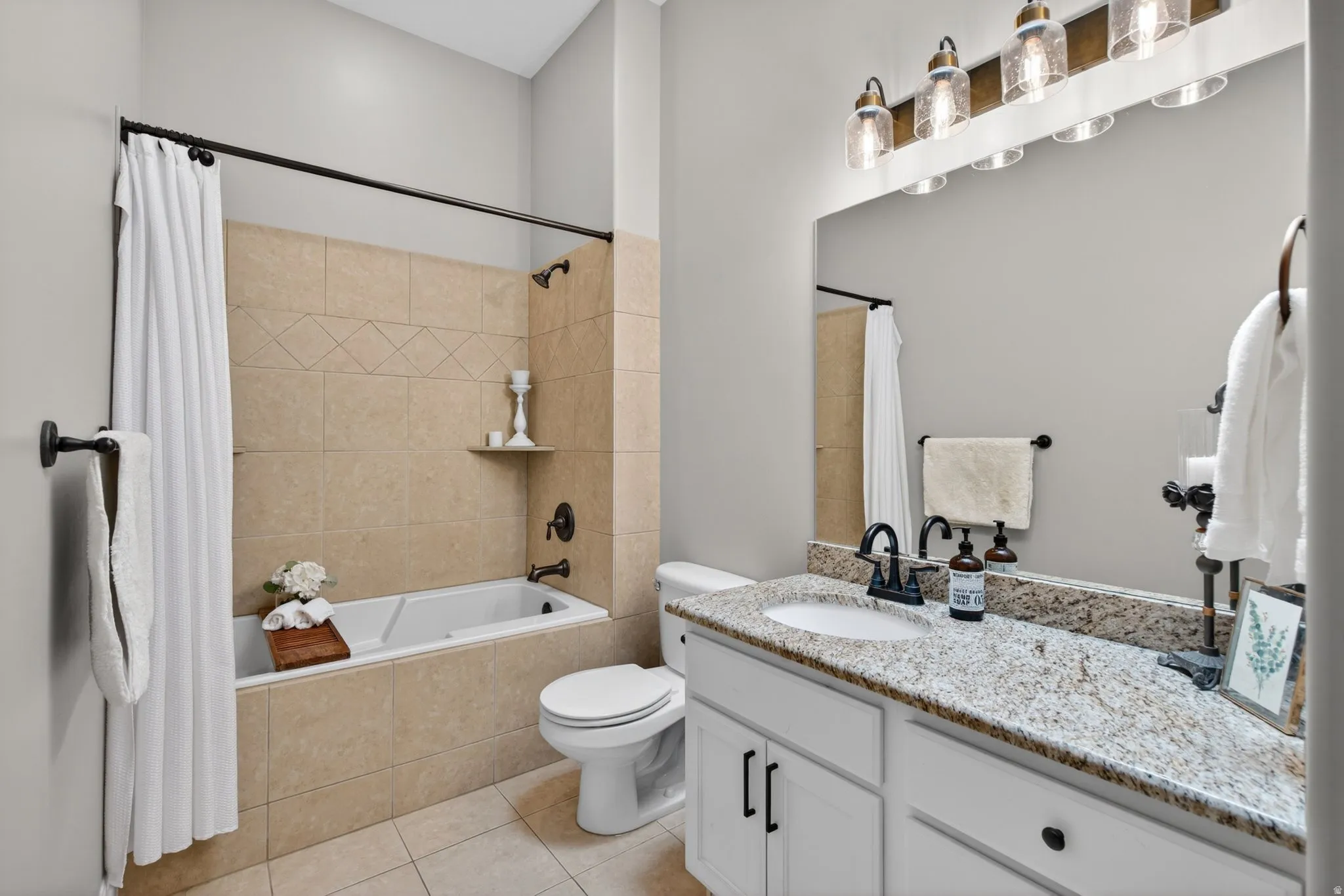 Bathroom featuring a spacious vanity with granite countertop, white cabinetry with dark hardware, and a large mirror