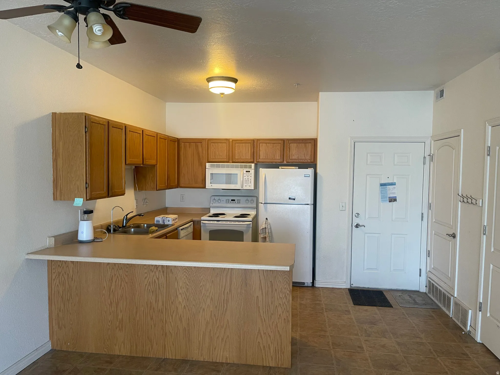 Kitchen featuring wood-finish cabinetry, white appliances, and a breakfast bar with a light-toned countertop