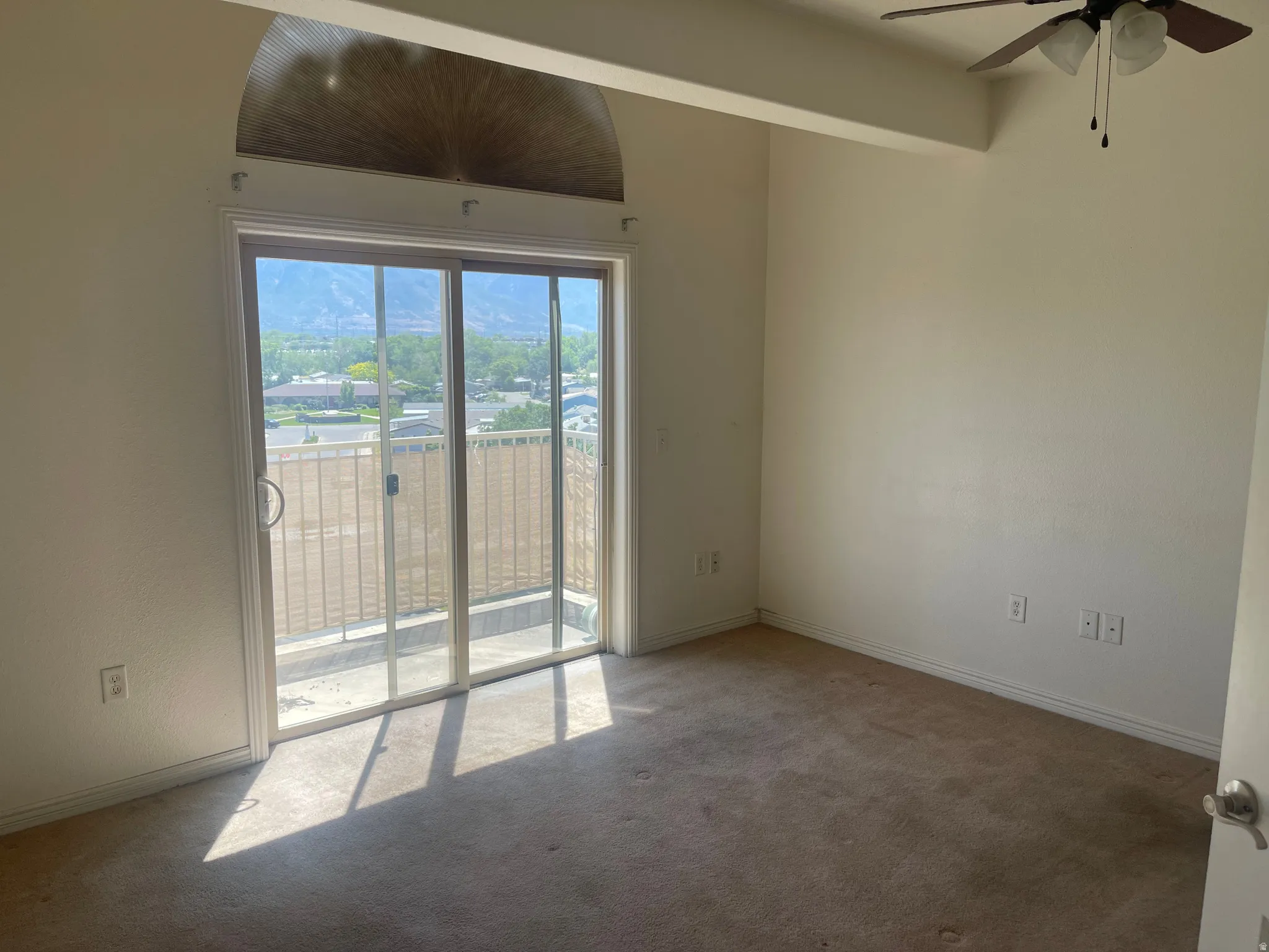 Carpeted room featuring a ceiling fan with light fixture, sliding glass door with balcony access, and an arched transom window