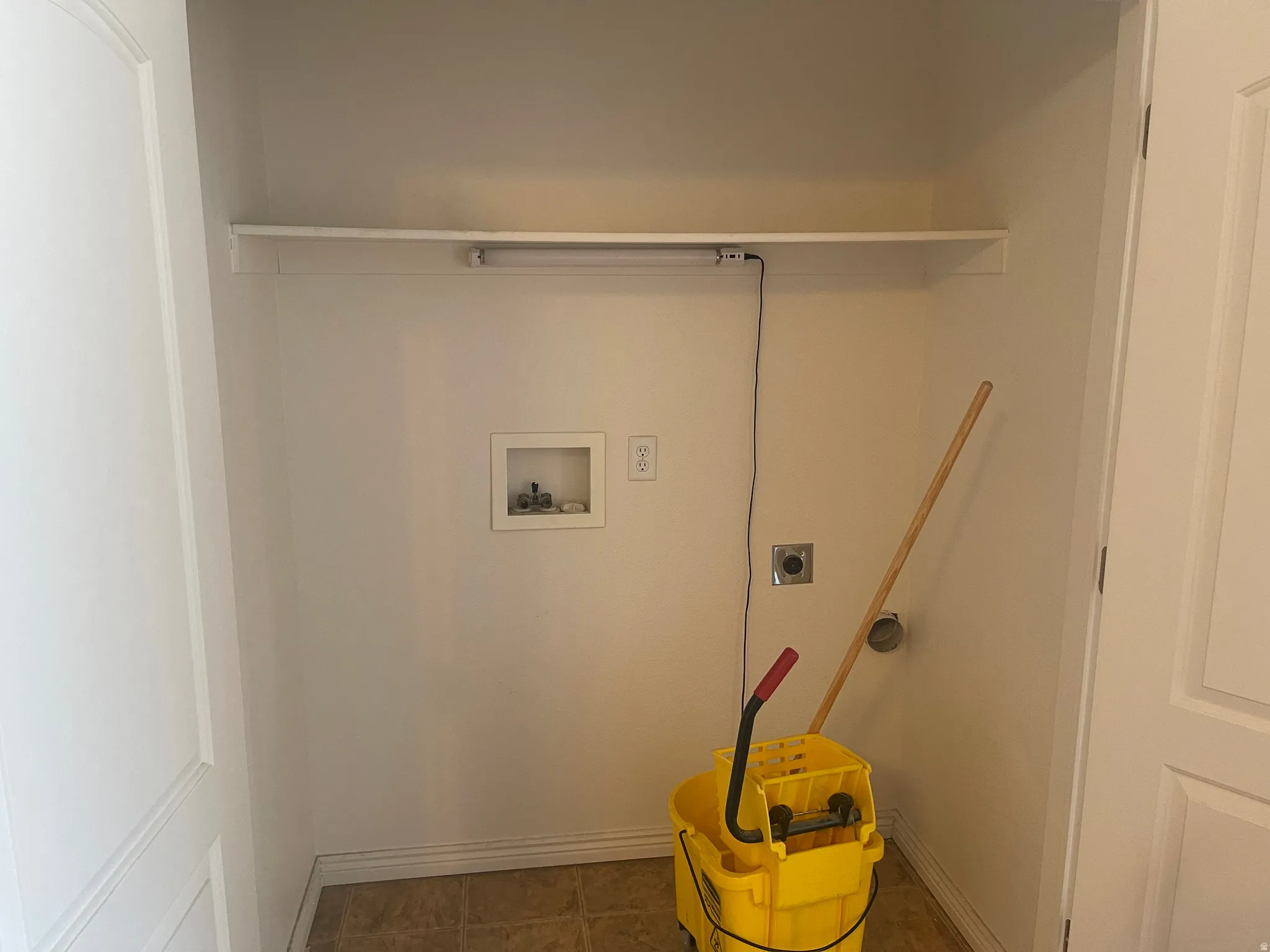 Dedicated utility alcove featuring a built-in shelf, plumbing hookups, electrical outlet, and floor drainage