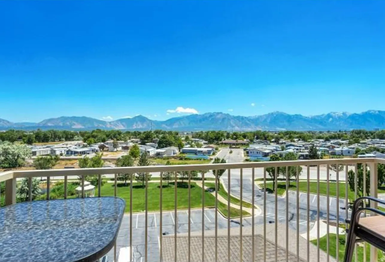 Balcony with a metal railing overlooking a landscaped green space, community buildings, and distant mountain ranges