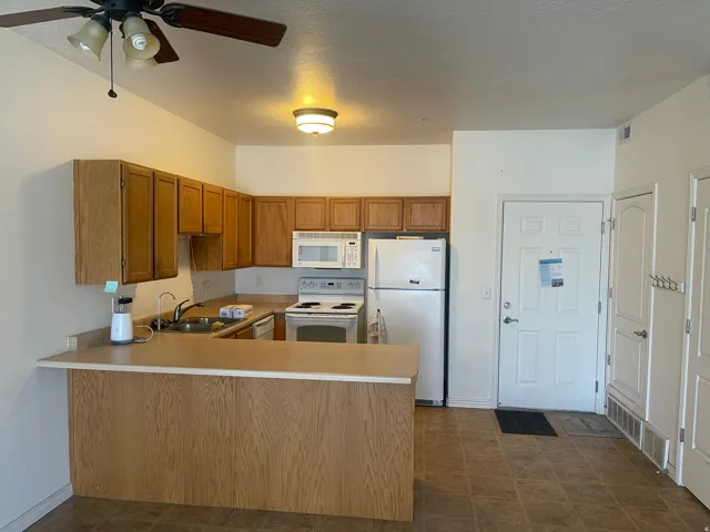 Kitchen featuring wood-finish cabinetry, white appliances, and a breakfast bar with a light-toned countertop