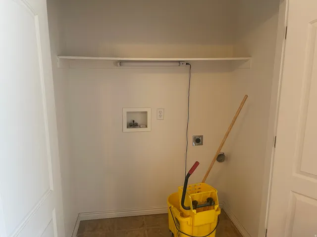 Dedicated utility alcove featuring a built-in shelf, plumbing hookups, electrical outlet, and floor drainage