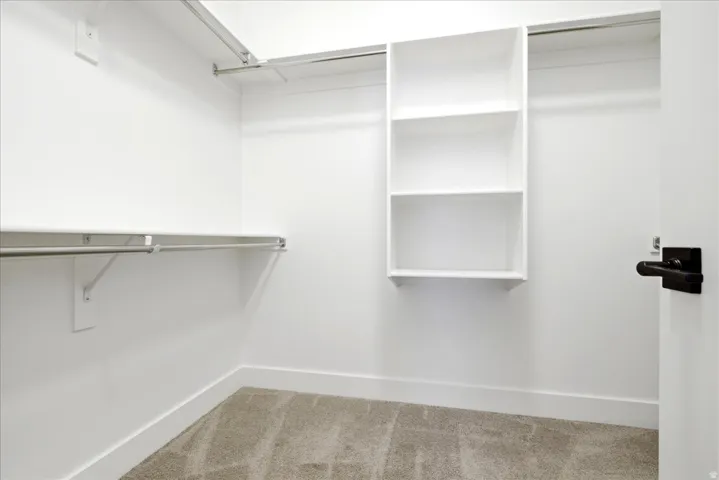 Walk-in closet featuring white walls, carpeting, white baseboards, and a black lever door handle
