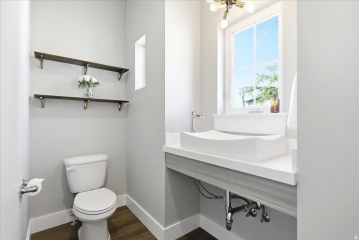 Contemporary bathroom featuring a unique vessel sink, single-handle faucet, window with exterior scenery, wood-finish flooring, and two wall-mounted shelves