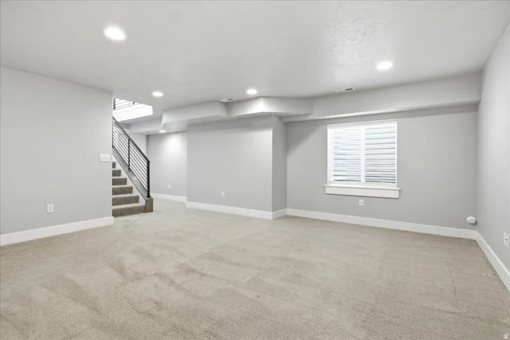 Spacious lower level featuring light gray walls, plush carpeting, recessed lighting, and a window with white blinds