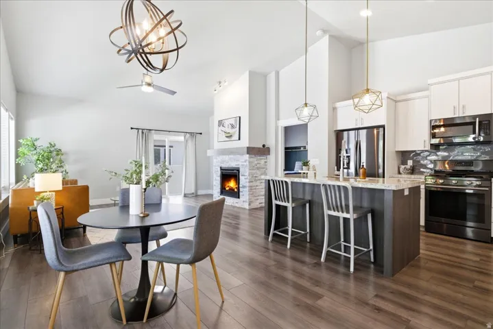 Open-concept living space featuring wood-finish flooring, a contemporary fireplace with stacked stone surround, and vaulted ceilings