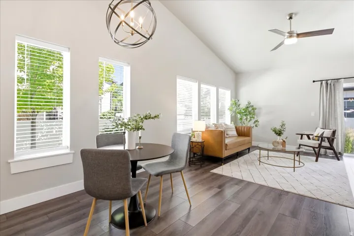 Interior featuring vaulted ceilings, wood-finish flooring, multiple windows with blinds, a contemporary ceiling fan, and a decorative orb chandelier