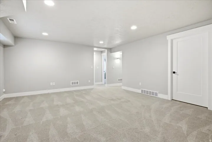 Spacious room featuring light gray walls, recessed ceiling lighting, textured light-toned carpet, white trim work, and a contemporary white panel door with black hardware