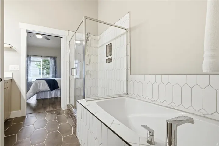 Bathroom featuring a built-in tub with modern fixtures, a glass-enclosed shower with white tiled walls, and hexagonal floor tiles