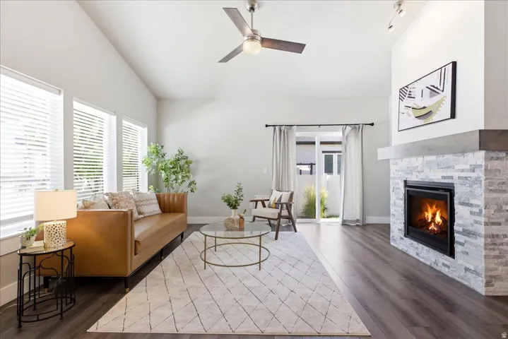 Spacious living area featuring vaulted ceilings, wood-finish flooring, a contemporary fireplace with a stone surround and wood mantel, and a sliding glass door providing exterior access