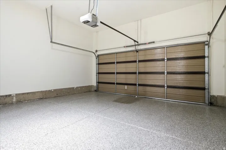 Expansive garage featuring an epoxy-coated concrete floor, a tan sectional garage door, white painted walls, and an overhead garage door opener system