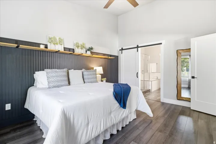 Vaulted ceiling bedroom featuring wood-finish flooring and a barn door entry to a bathroom with a glass-enclosed shower