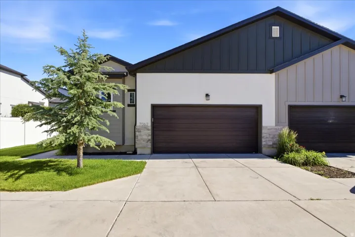 Contemporary facade featuring a dark brown garage door, light stucco, vertical siding accents, and stone detailing