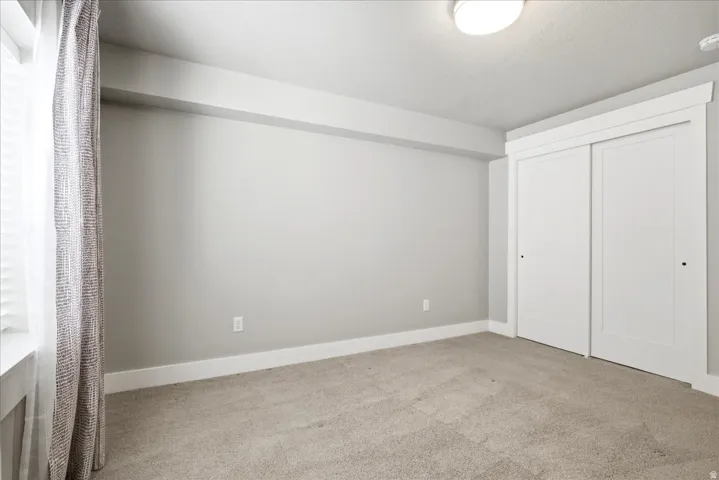 Interior room featuring light gray walls, plush carpeting, a large window with blinds, and a built-in closet with sliding white doors
