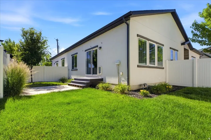 Expansive lawn and patio area featuring a white vinyl fence, mature trees, and landscaping