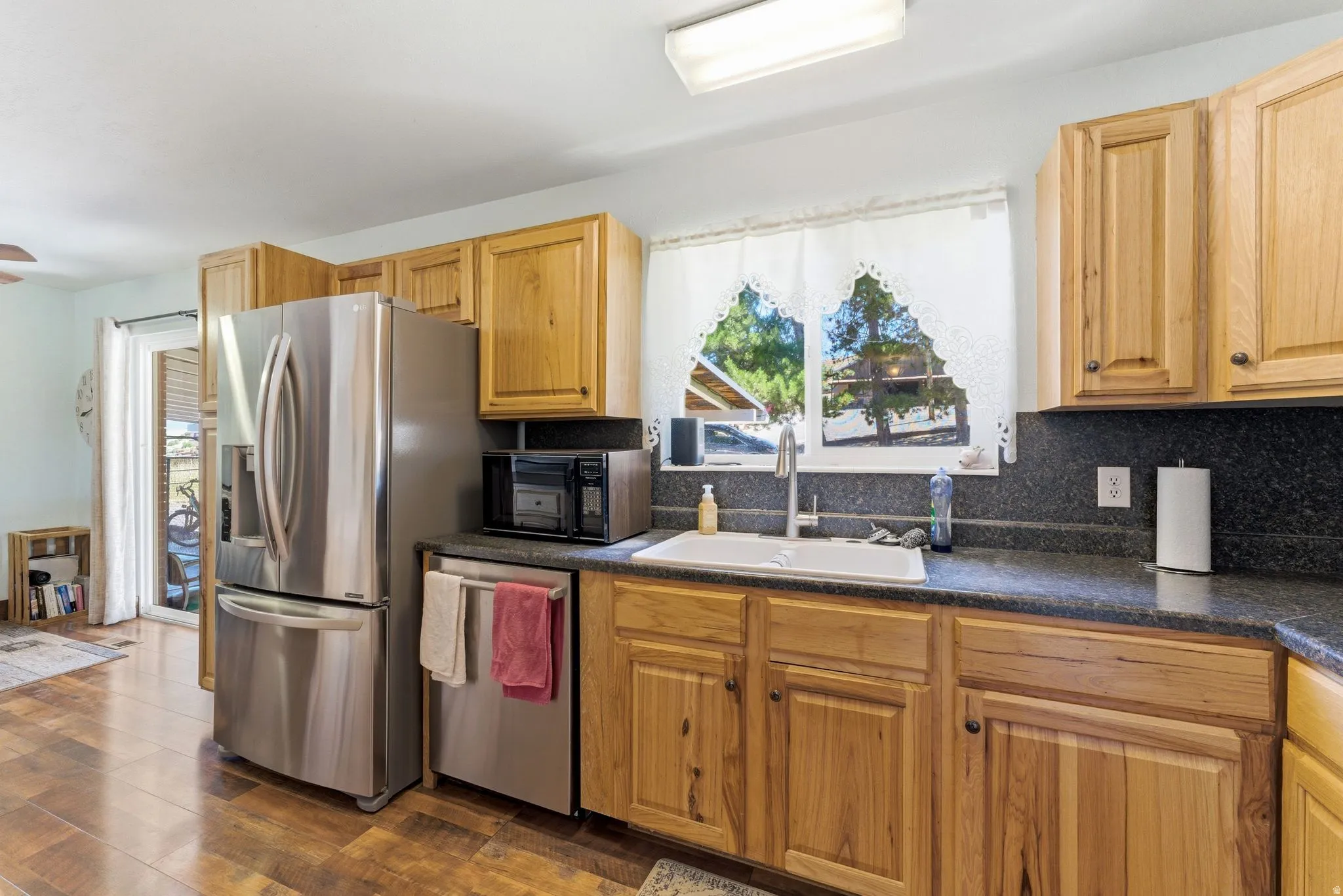 Kitchen featuring wood-finish flooring, natural wood cabinetry, dark speckled countertops, a white undermount sink with a gooseneck faucet, and stainless steel appliances