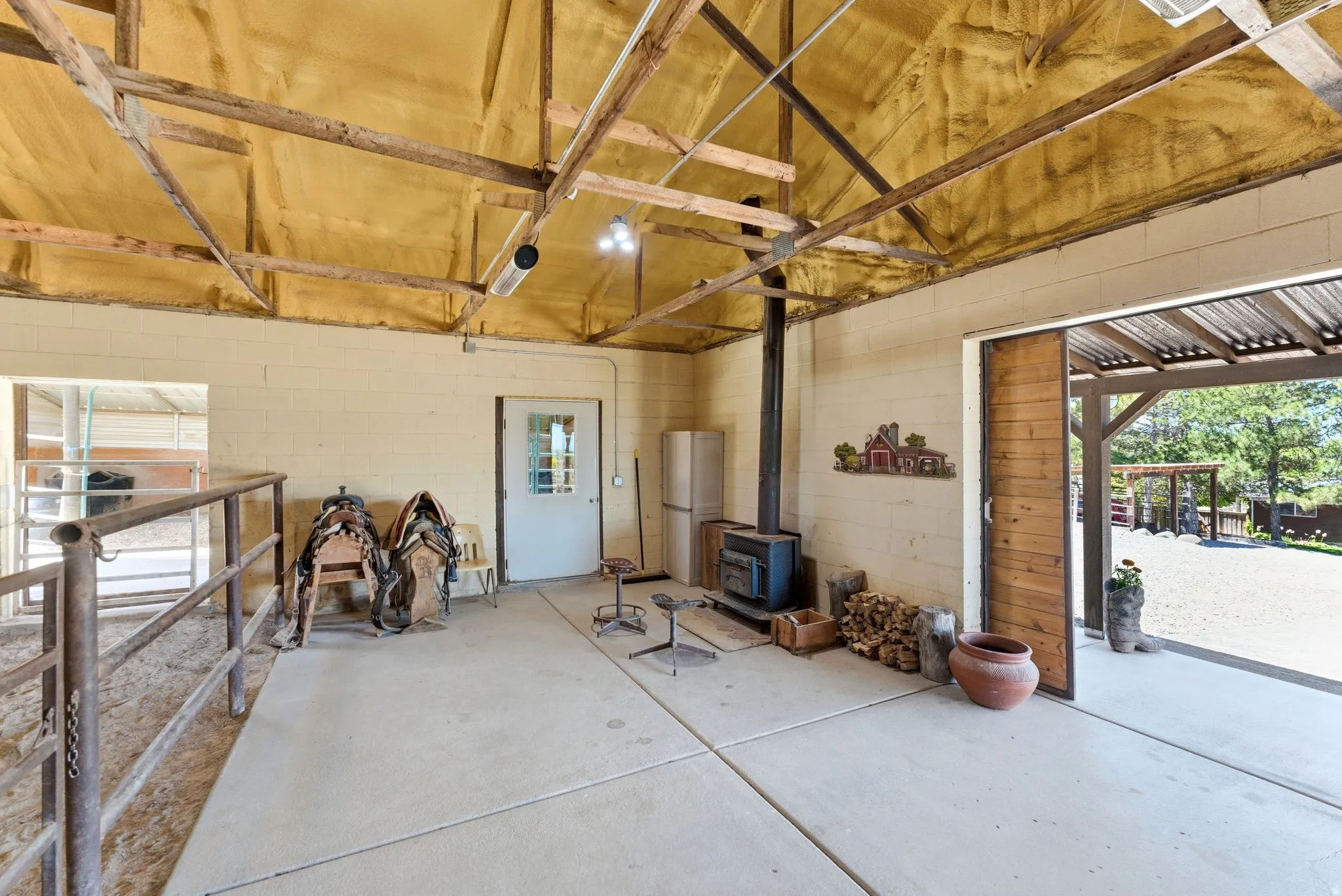 Spacious barn interior featuring concrete flooring, exposed wood beam ceiling, a wood-burning stove, and a large sliding wood barn door