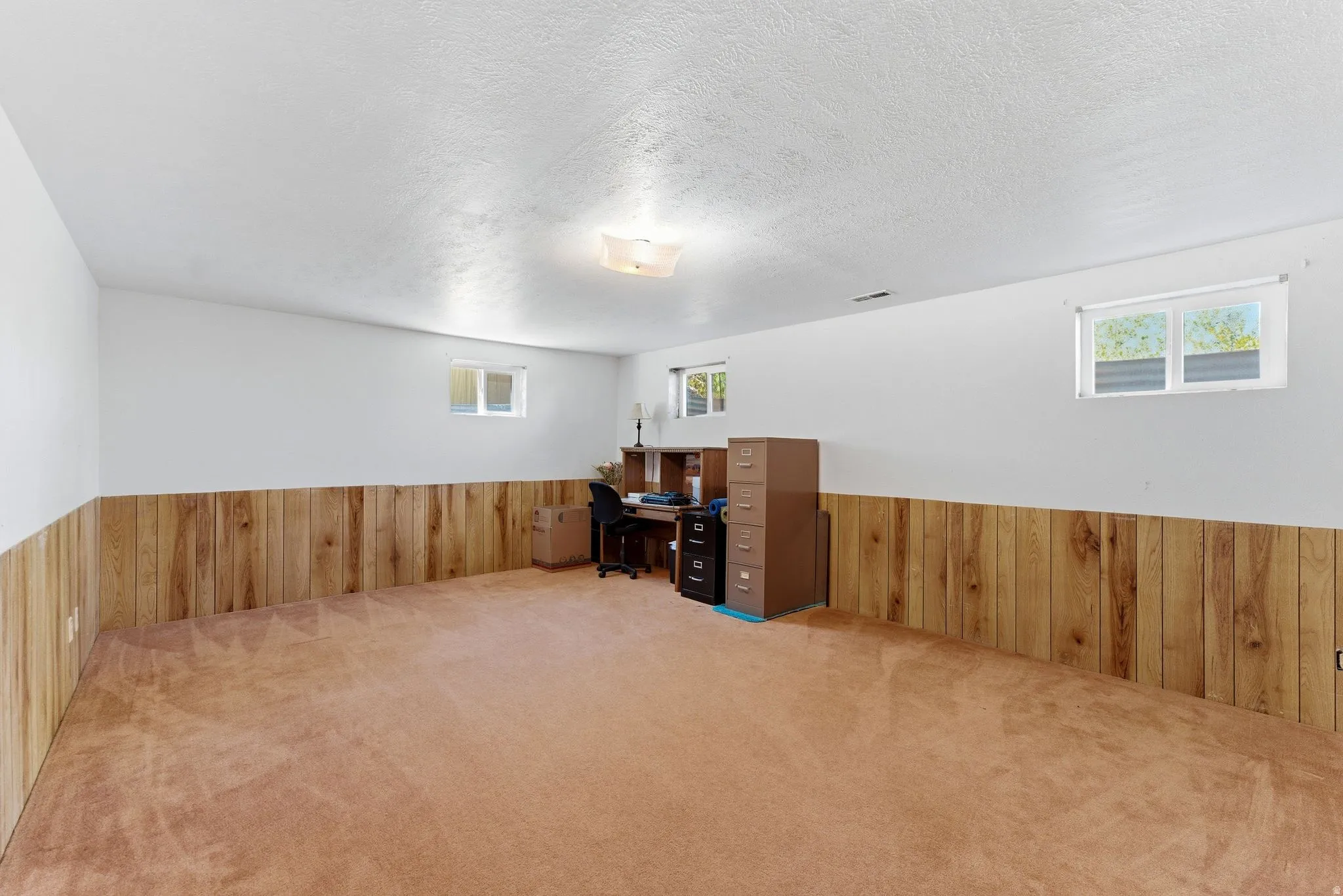 Spacious room featuring carpeting, wood paneling, white walls, and multiple windows