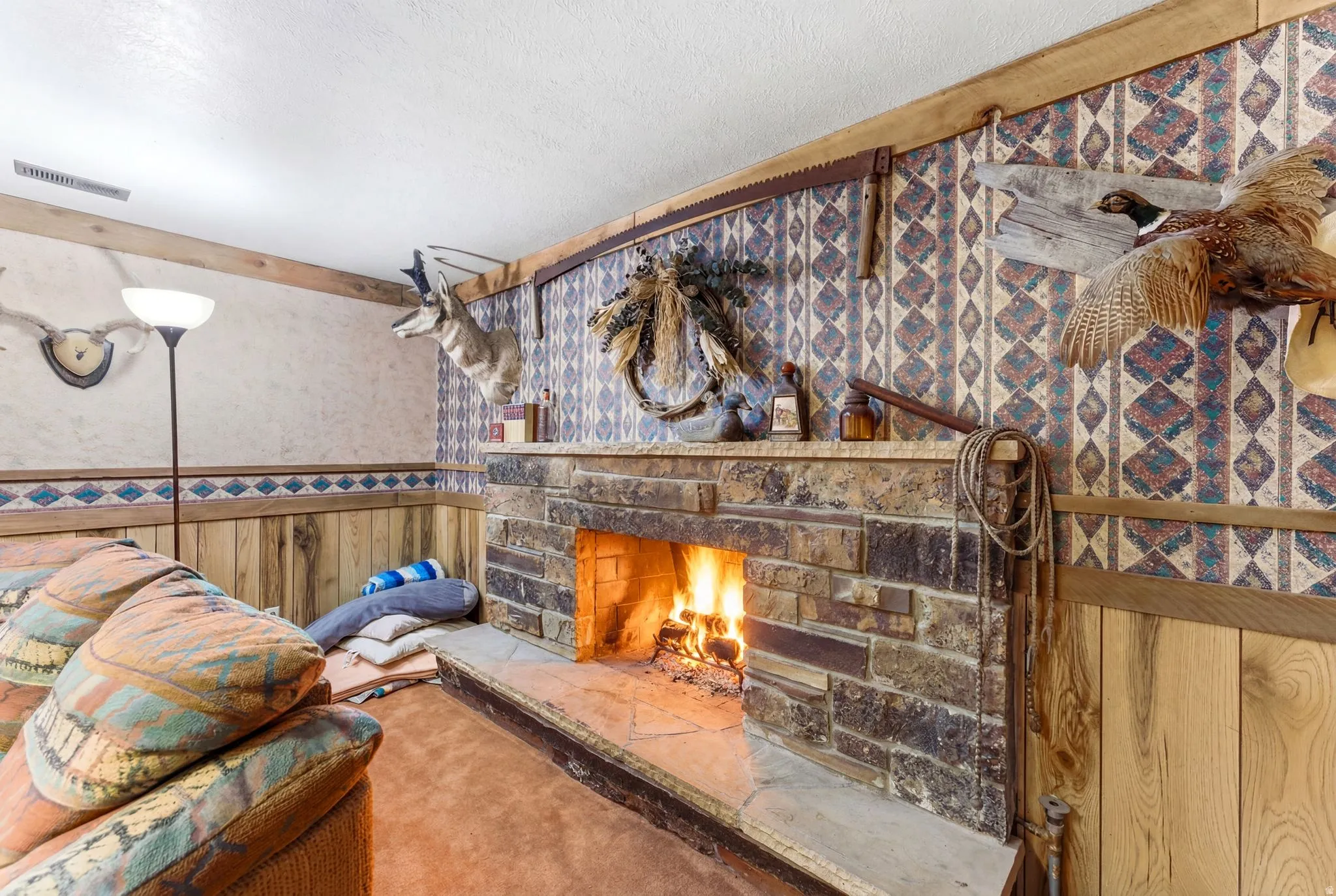 Stone-clad fireplace with a hearth and mantel, complemented by wood paneling and patterned wallpaper