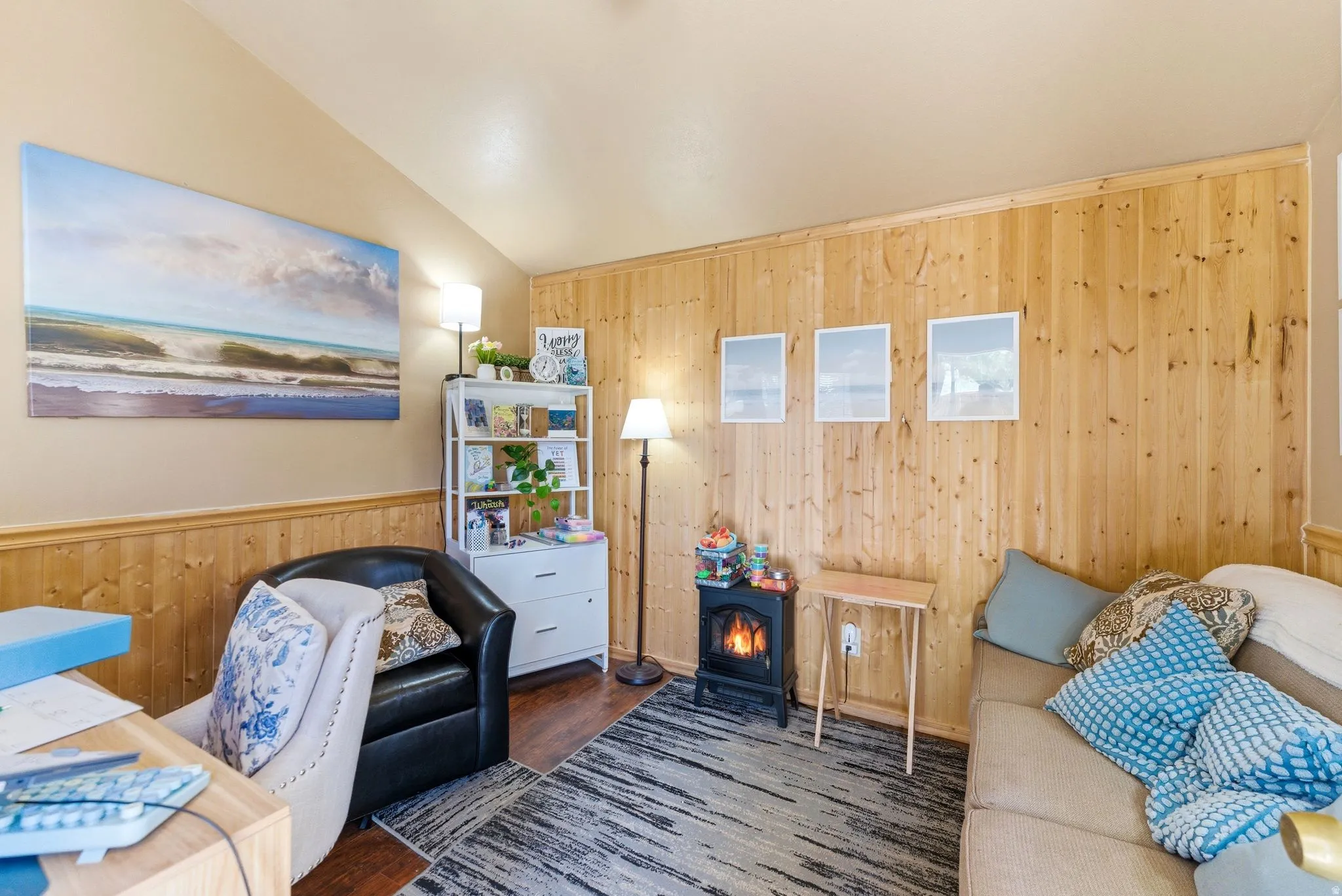 Room featuring a vaulted ceiling, wood-finish flooring, and a prominent wood-paneled accent wall with a matching chair rail