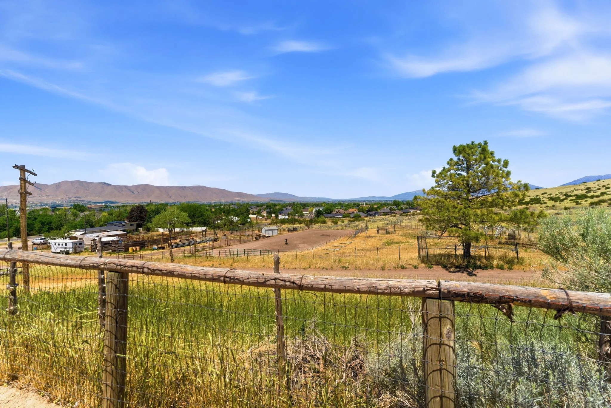 Expansive landscape featuring a rustic wood and wire fence, mature pine trees, and distant mountains