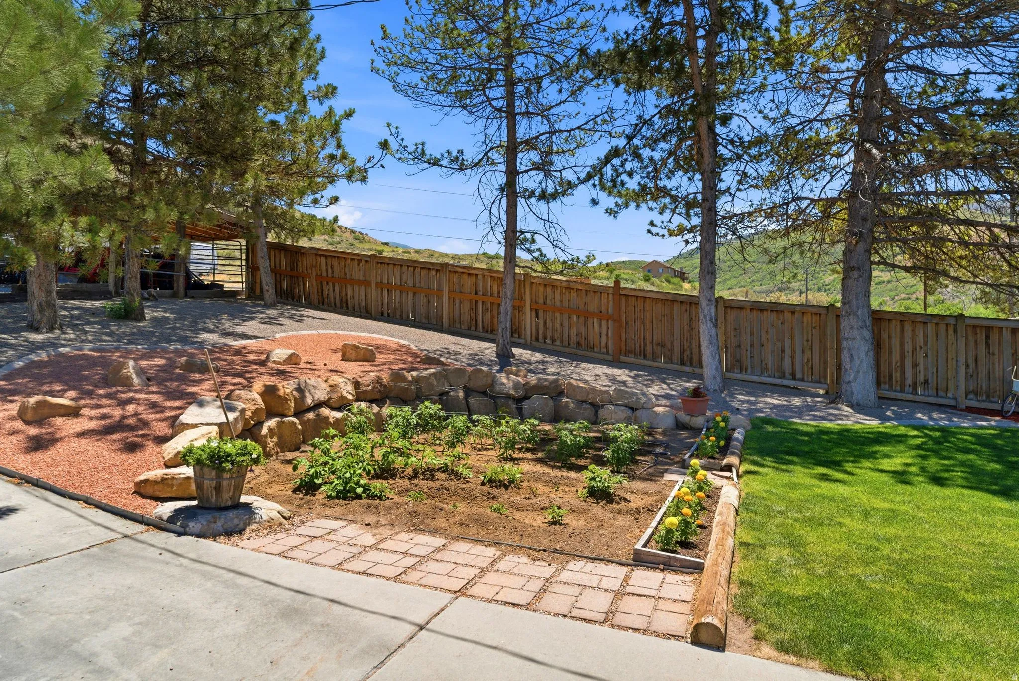 Landscaped garden beds with a stone retaining wall, brick paver accents, and mature trees