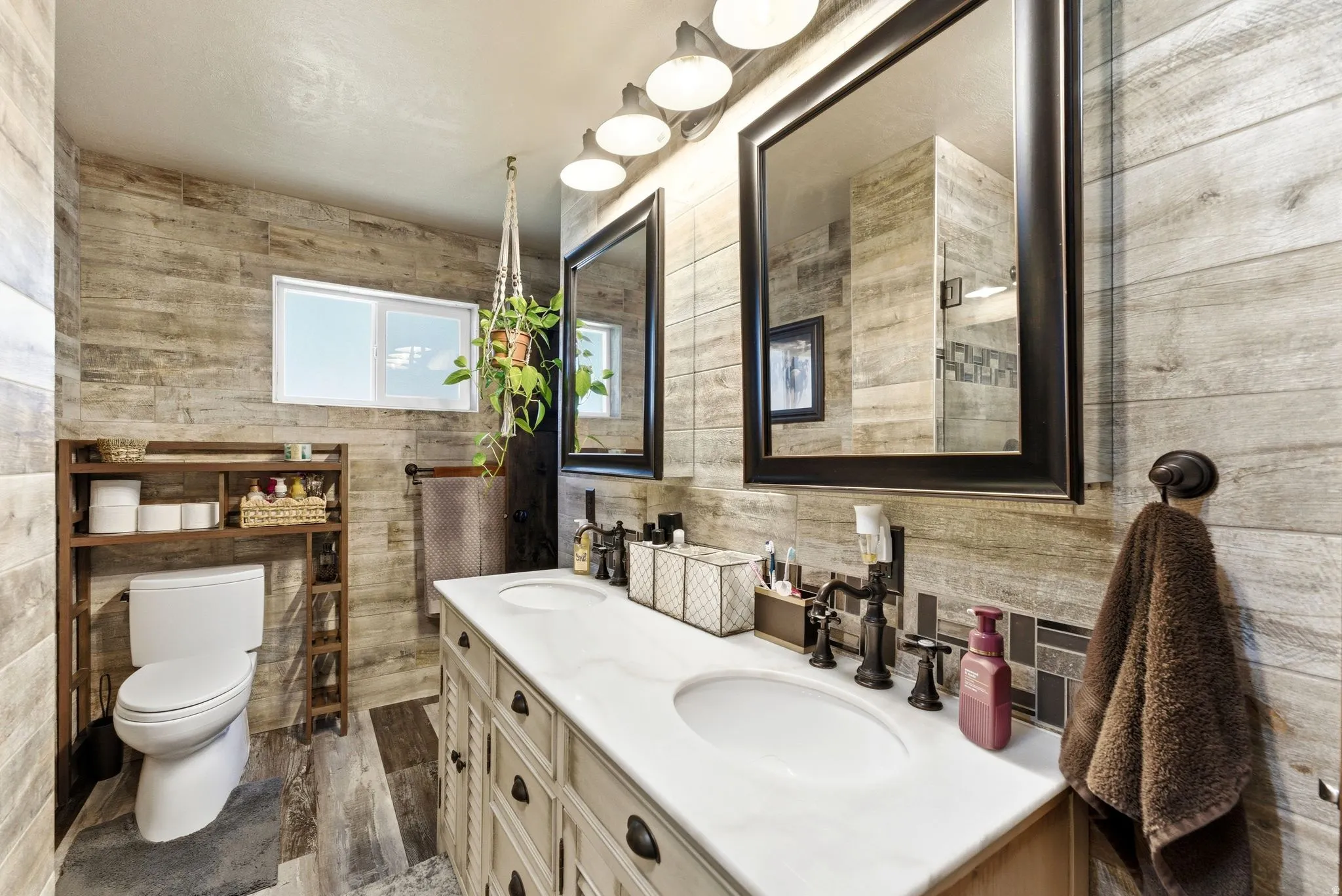 Dual vanity with undermount sinks and dark bronze fixtures set against wood-look tile walls