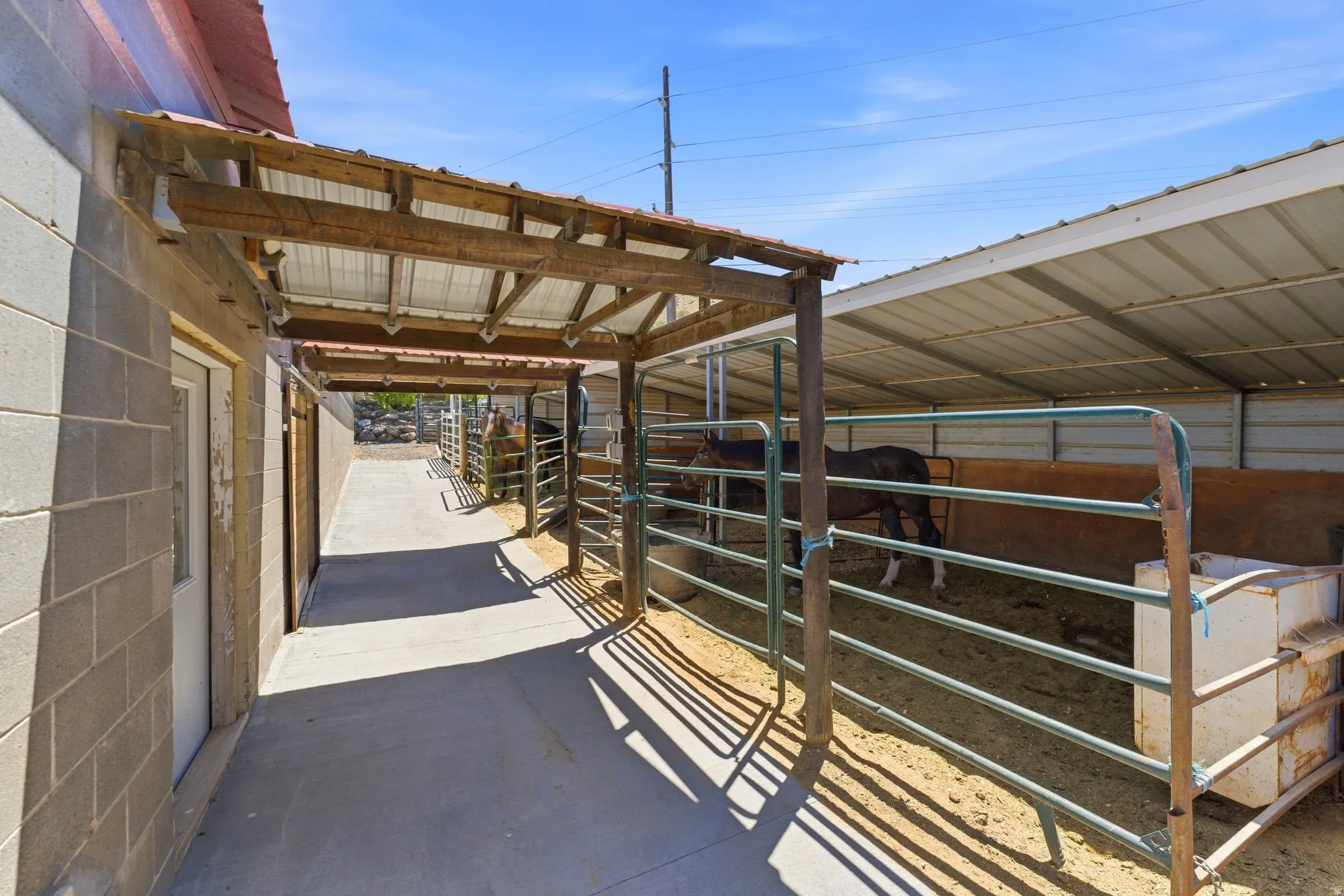 Covered walkway alongside a block structure, leading to a fenced animal enclosure with a metal roof