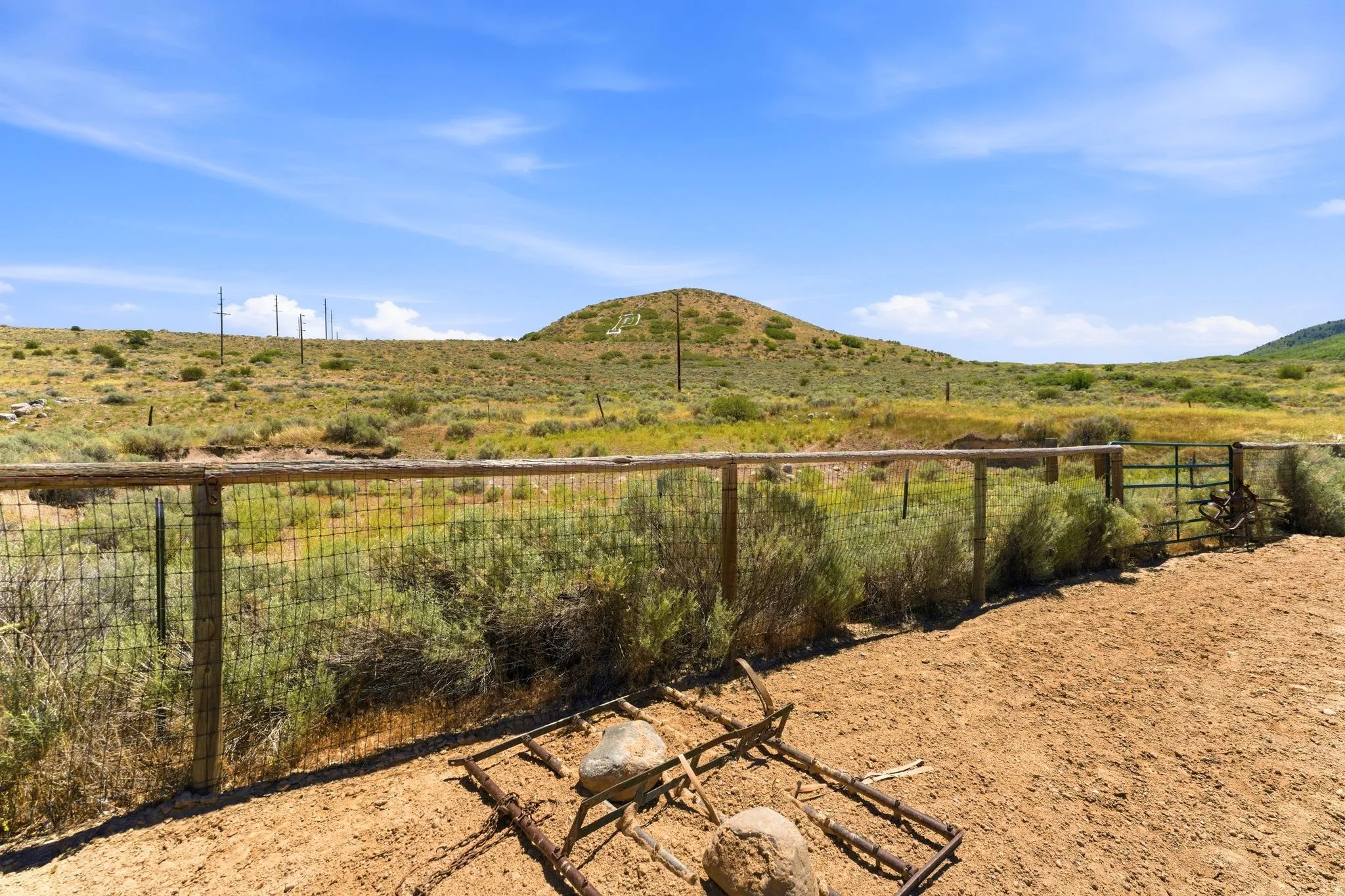 Fenced outdoor area with a metal gate and natural wood-finish posts, featuring a dirt ground surface