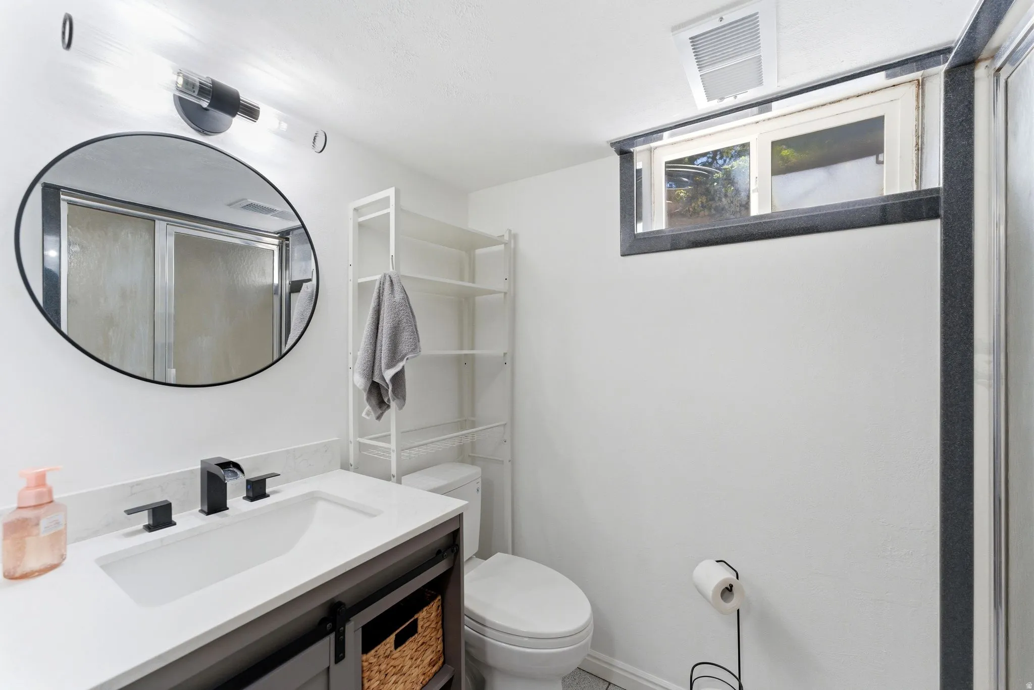 Bathroom featuring a single vanity with dark cabinetry and white countertop, black fixtures, an oval mirror, and a shower with a sliding glass door