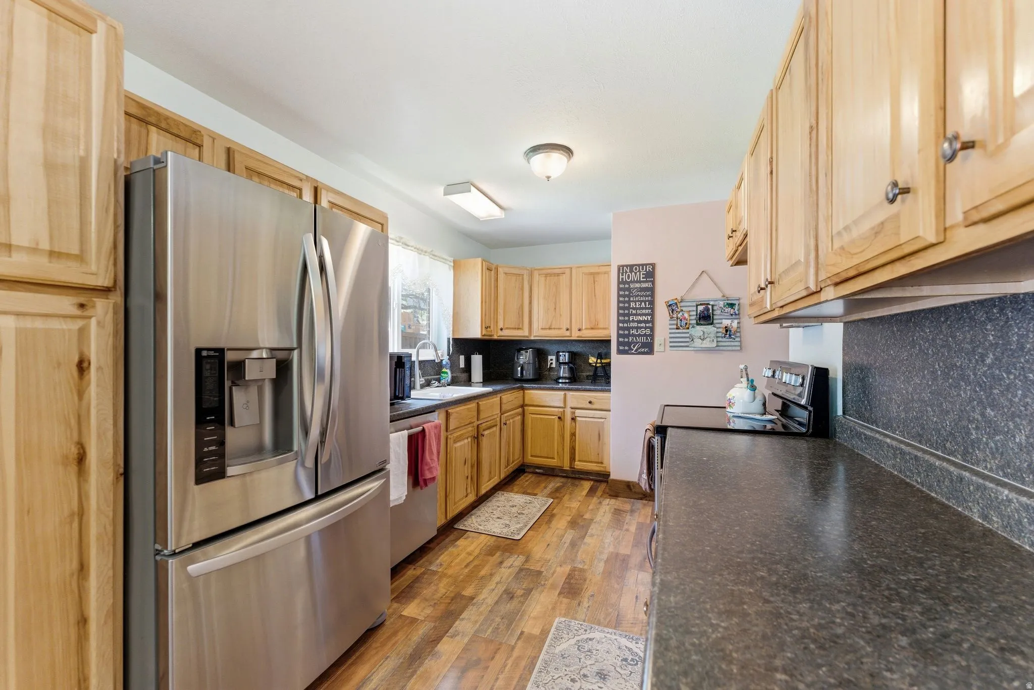 Kitchen featuring wood-finish flooring, light wood cabinetry, dark countertops, and stainless steel appliances