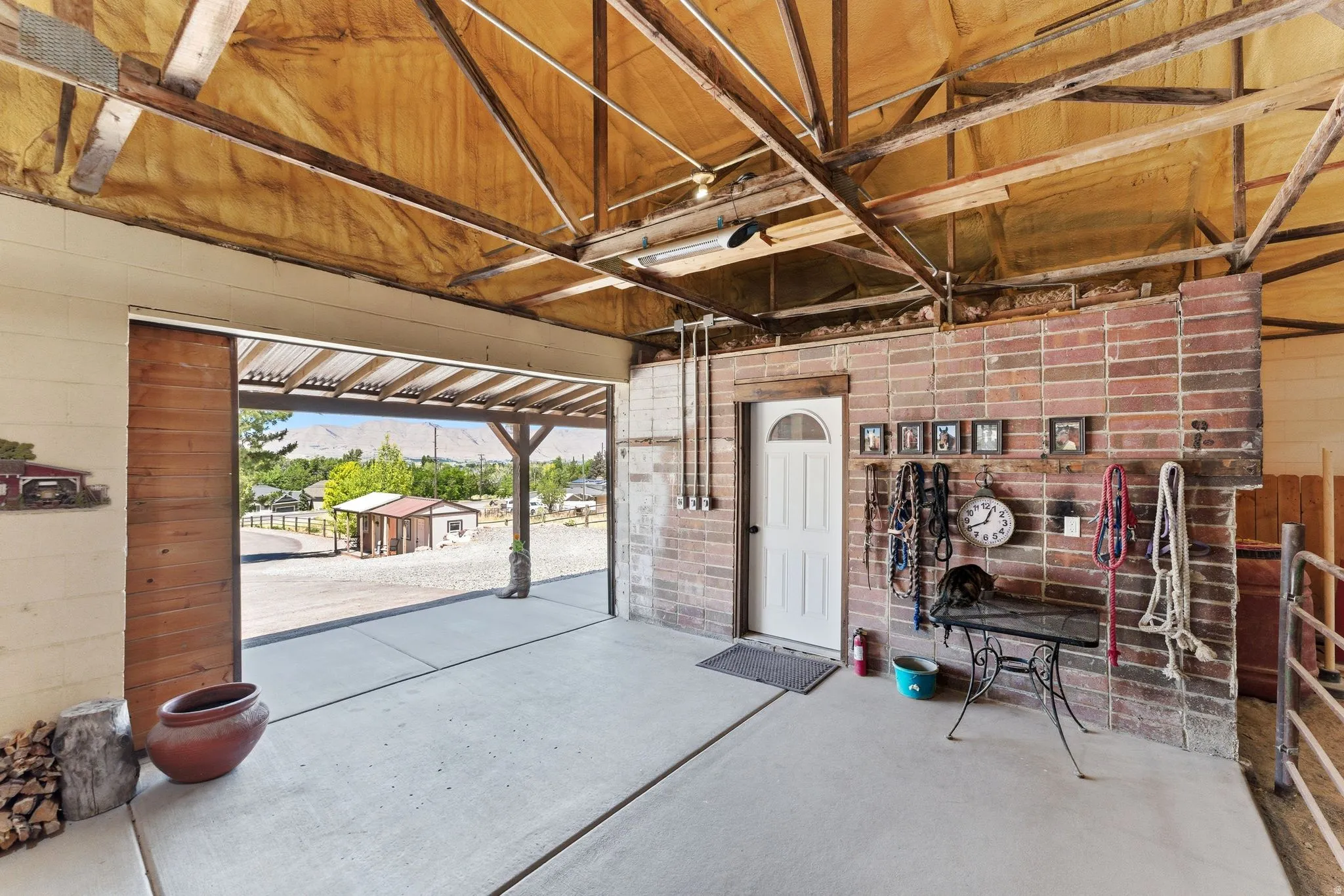 Open-air barn structure featuring exposed wood rafter ceiling, concrete flooring, a brick accent wall, and a large sliding wooden door