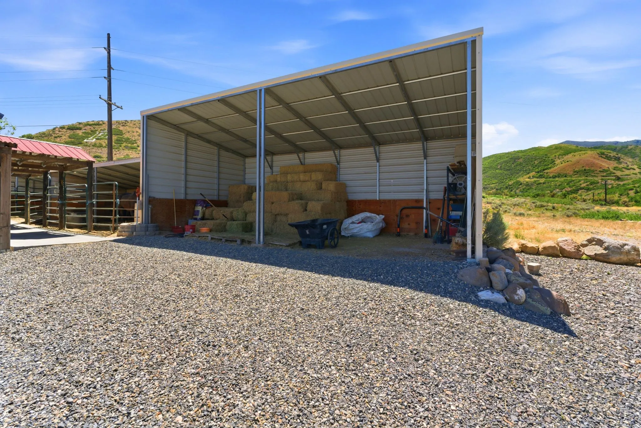 Gravel driveway leading to a metal-frame storage shed with an open-sided design