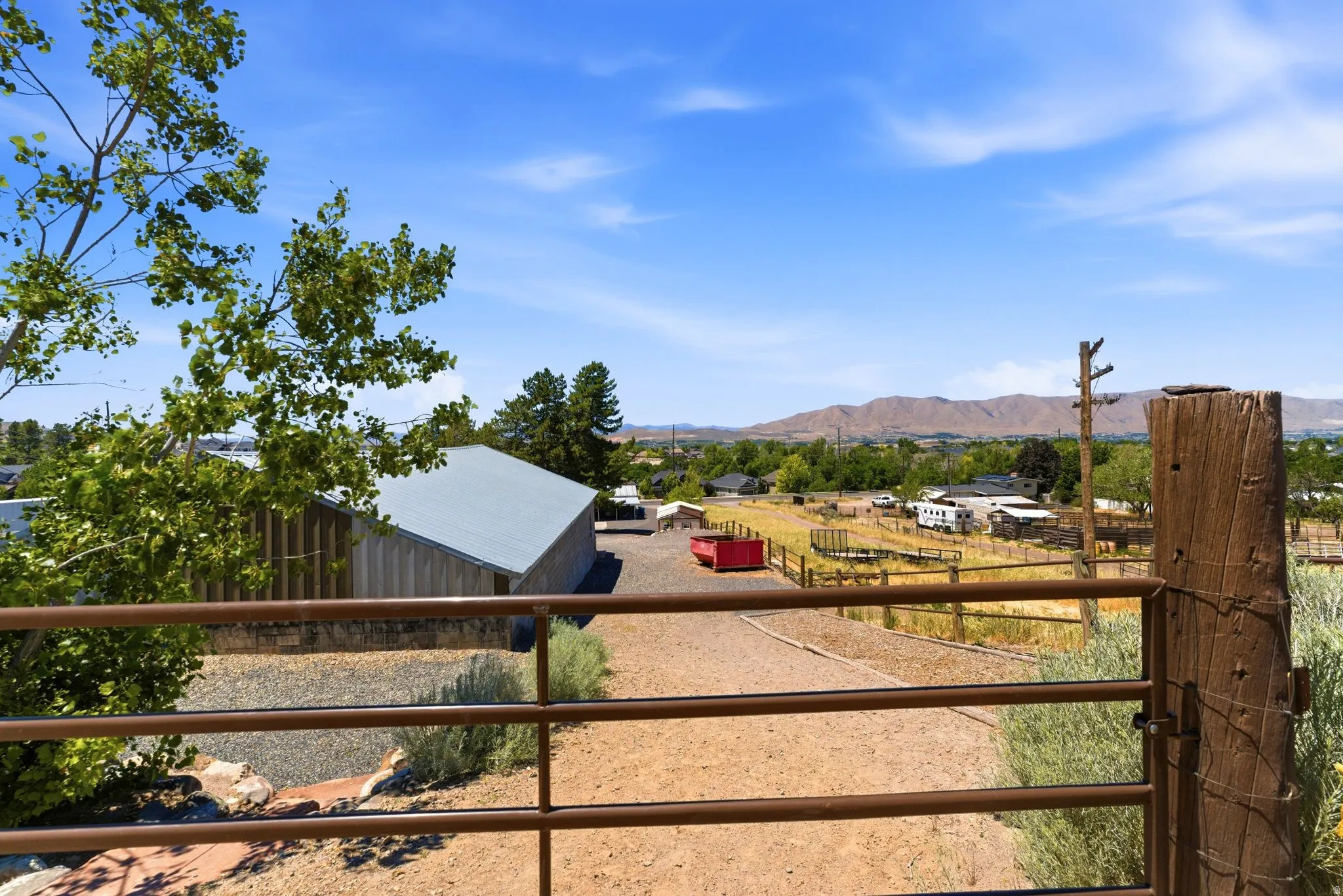 Ranch-style property featuring a metal gate entrance, a gravel driveway, and a wood-sided outbuilding with a metal roof