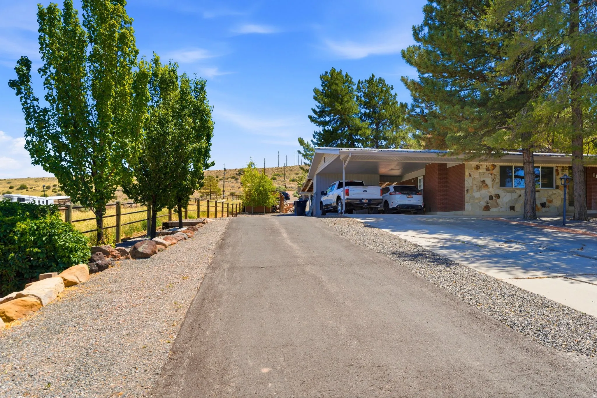 Paved driveway with gravel borders, mature trees, and a wooden fence