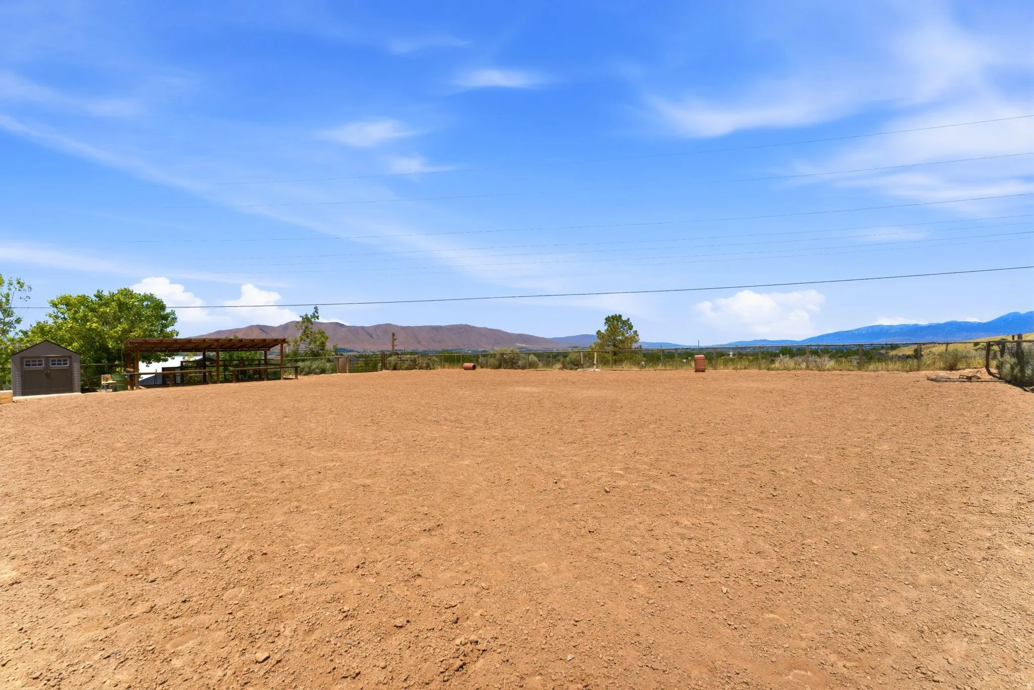Spacious open lot featuring a covered patio structure, detached storage shed, perimeter fencing, and distant mountain scenery